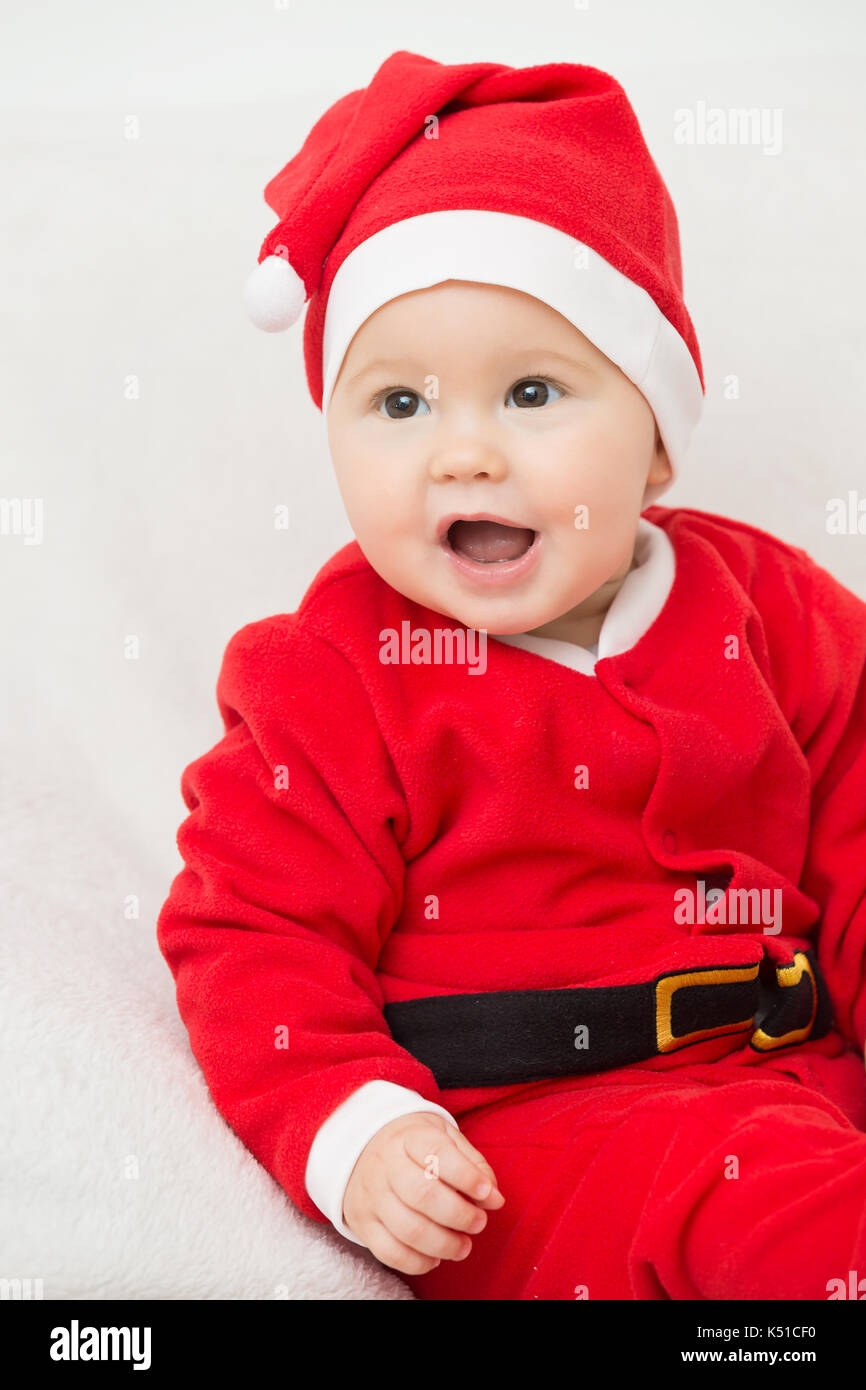 Seven months old baby girl in Santa Claus dress sitting on a white