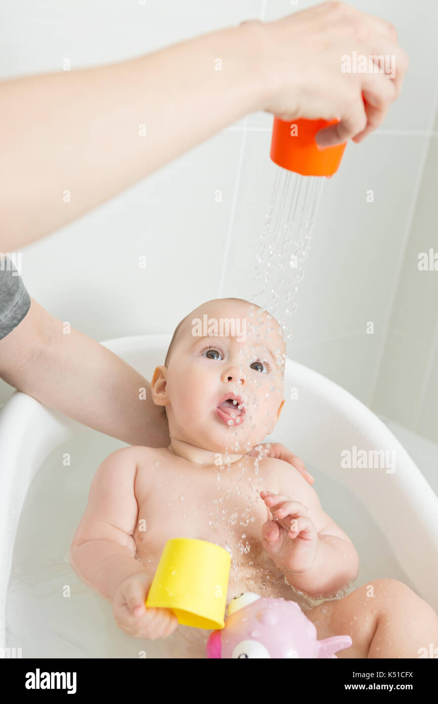 Seven months old baby girl in a bath, playing with pink toy and mothers