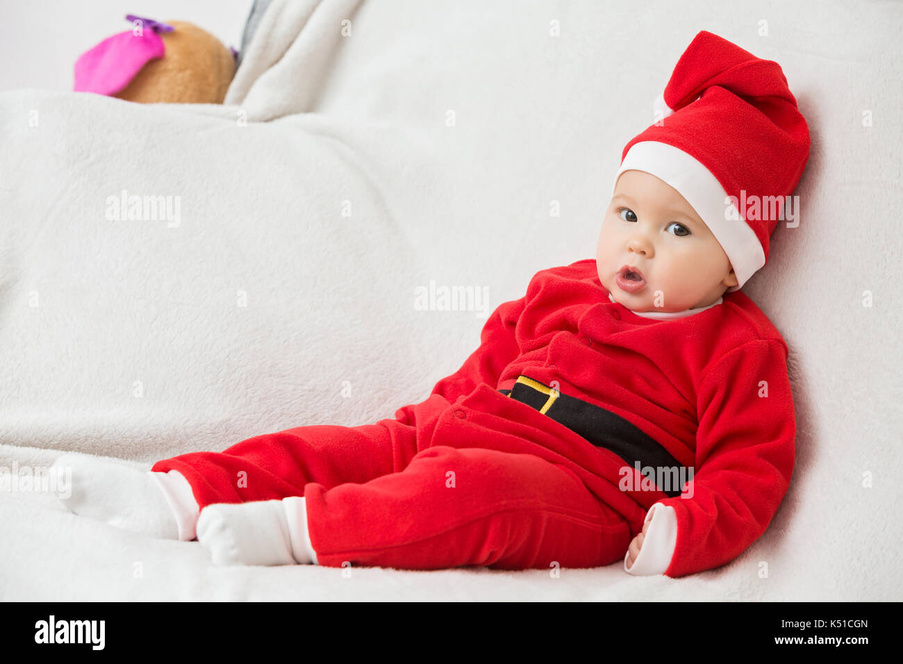 Seven months old baby girl in Santa Claus dress sitting sideways on a