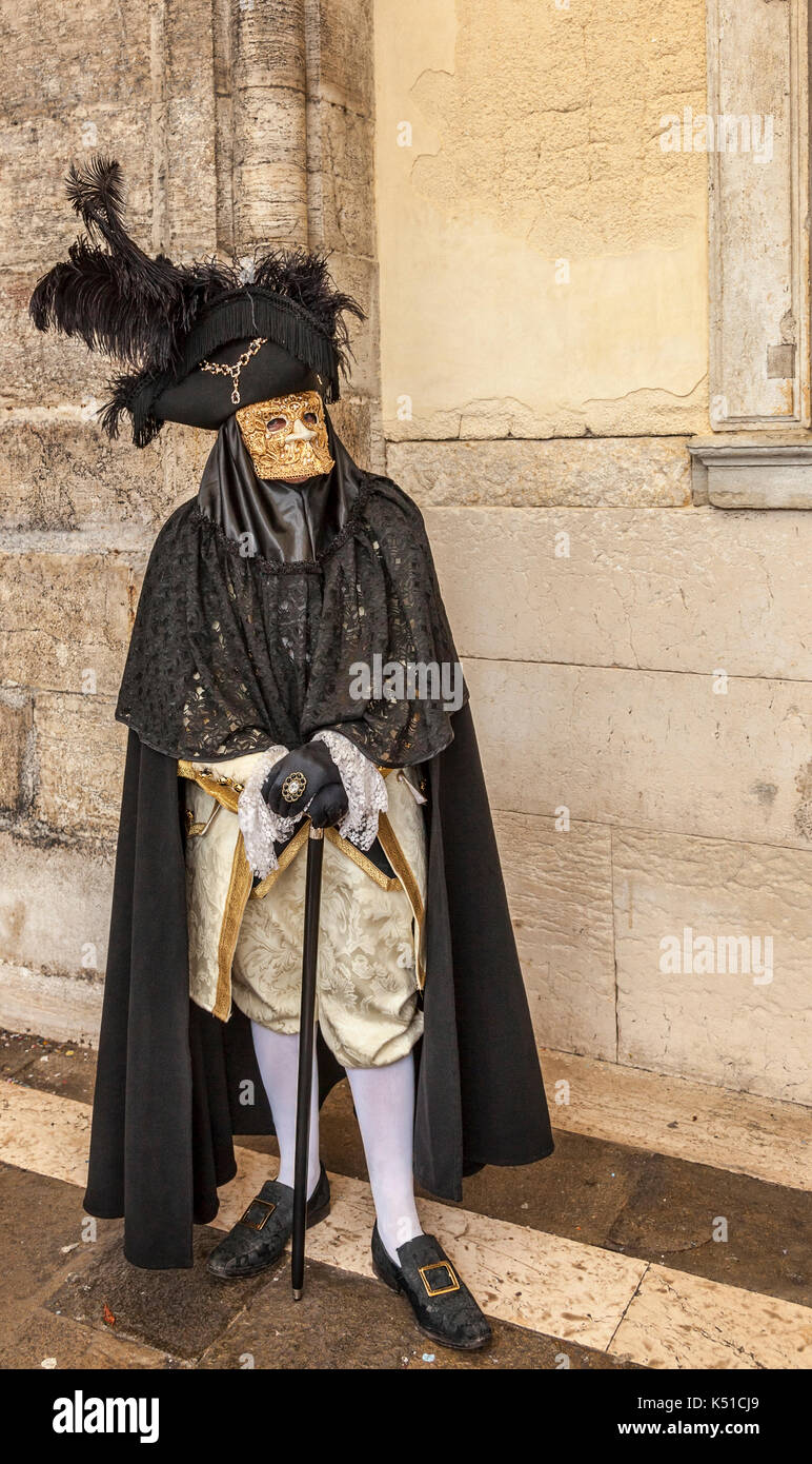 Venice, Italy- March 02, 2014: Unidentififed person specifically disguised wearing a Bauta mask poises near the walls of The Doges Palace in Venice du Stock Photo