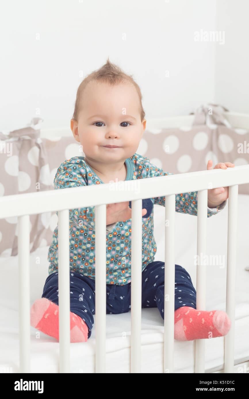 Eight months old baby girl sitting in her bed smiling and looking at the camera Stock Photo Alamy