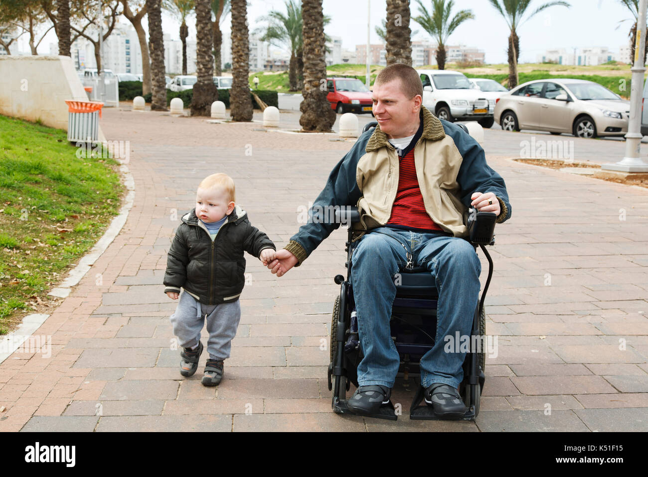 Dad walks in a wheelchair with a young son Stock Photo