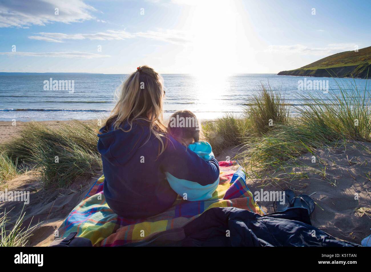 A mother and daughter on a beach at sunset cuddling Stock Photo
