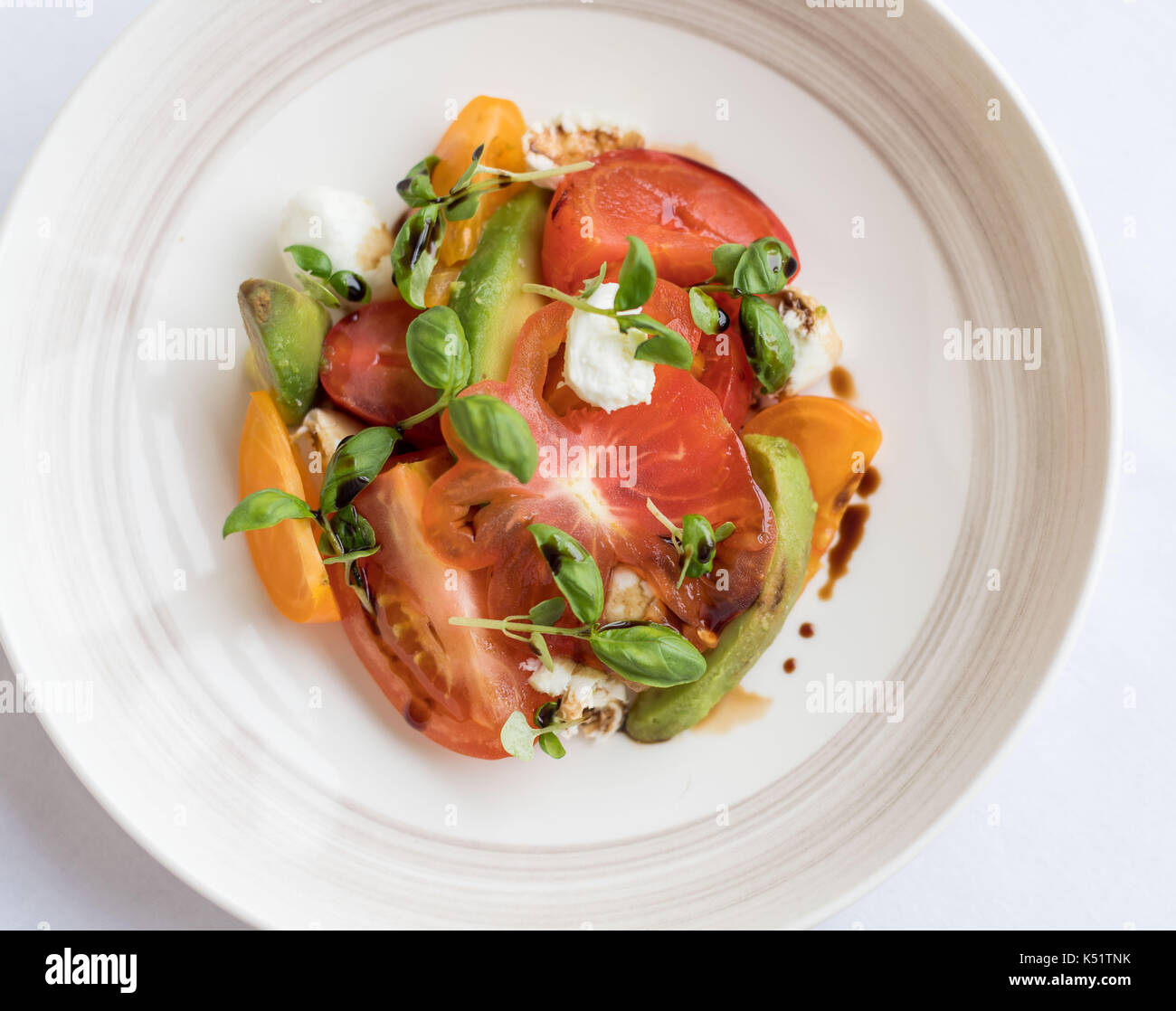 A tomato sald with basil and balsalmic vinegar on a white plate and white tablecloth Stock Photo