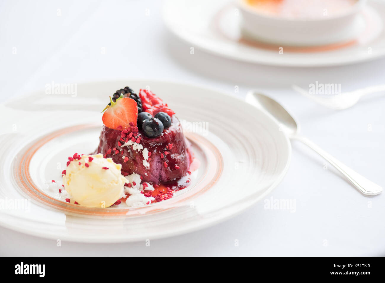 Summer fruit pudding with ice cream on a white plate and white tablecloth Stock Photo