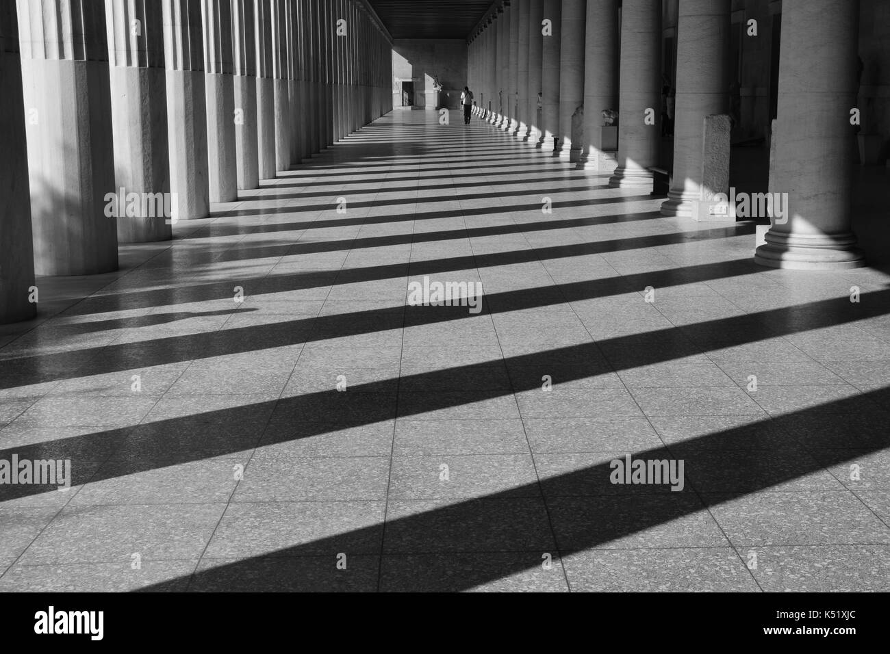 ATHENS, GREECE - OCTOBER 14, 2015: Man walking among the columns of stoa attalos at the ancient agora. Light and shadow abstract architecture black an Stock Photo