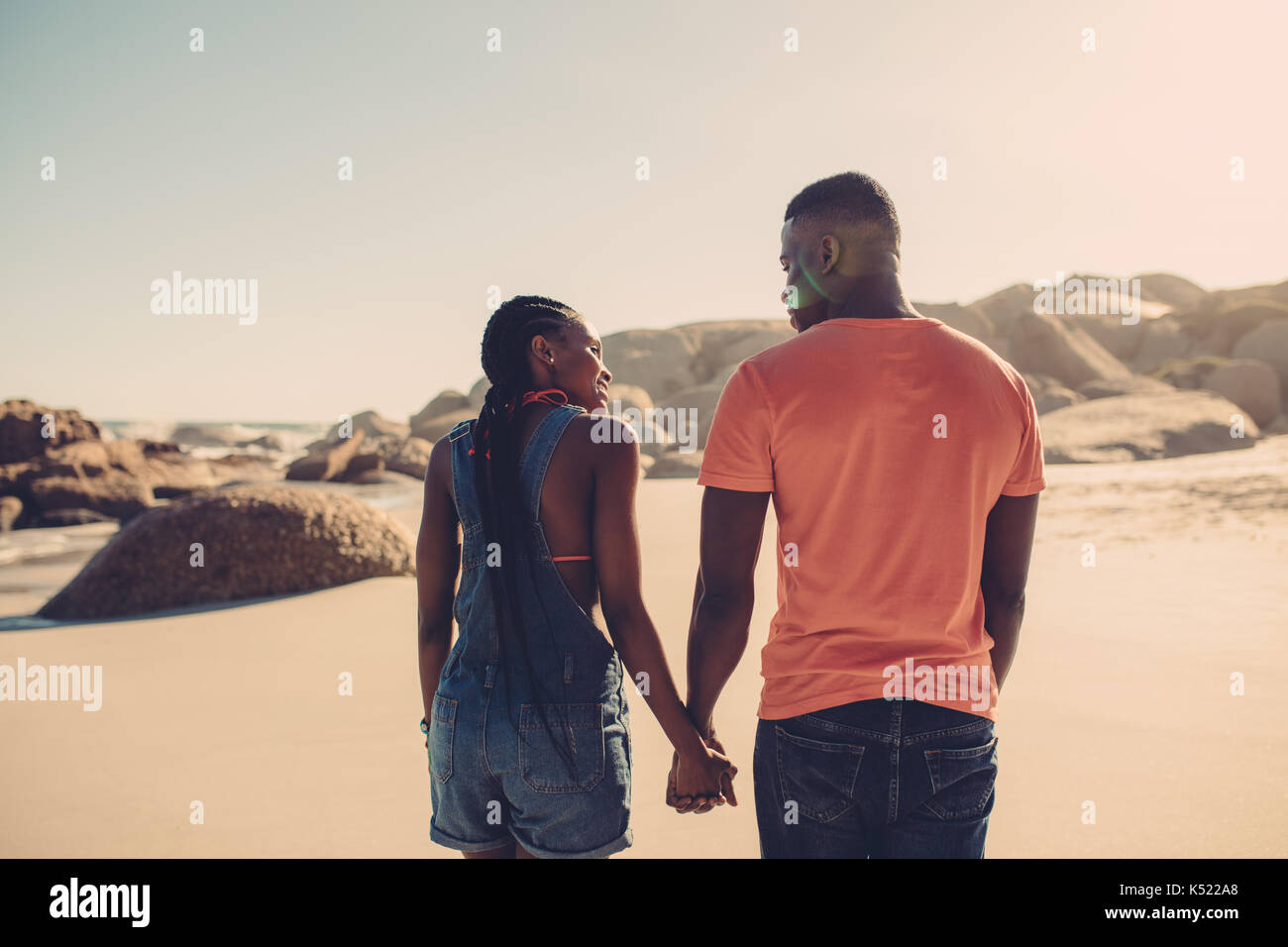 African american couple holding hands and walking along the beach. Man ...