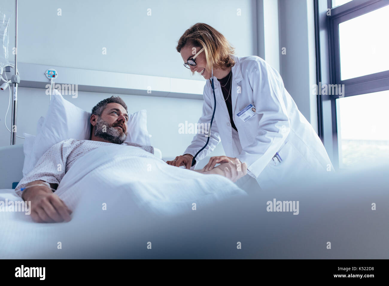 Hospitalized man lying in bed while doctor checking his pulse. Female physician examining male patient in hospital room. Stock Photo