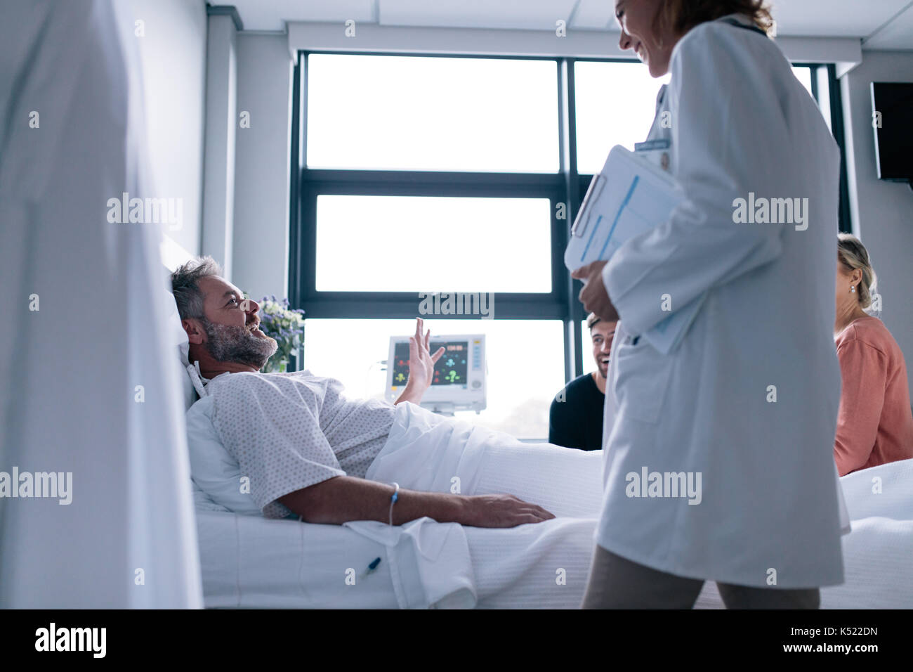 Female doctor visiting patient in hospital room. Sick man lying in bed