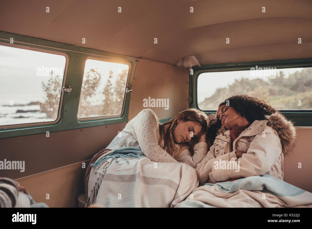 Two women friends on road trip sleeping inside the van. Female friends asleep in back seat of car while travelling. Stock Photo