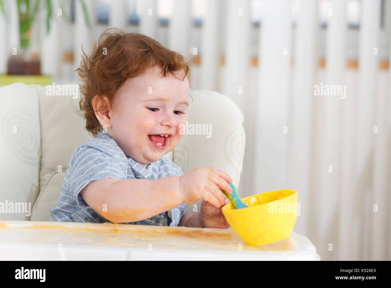Cute baby boy eating by himself on high chair Stock Photo