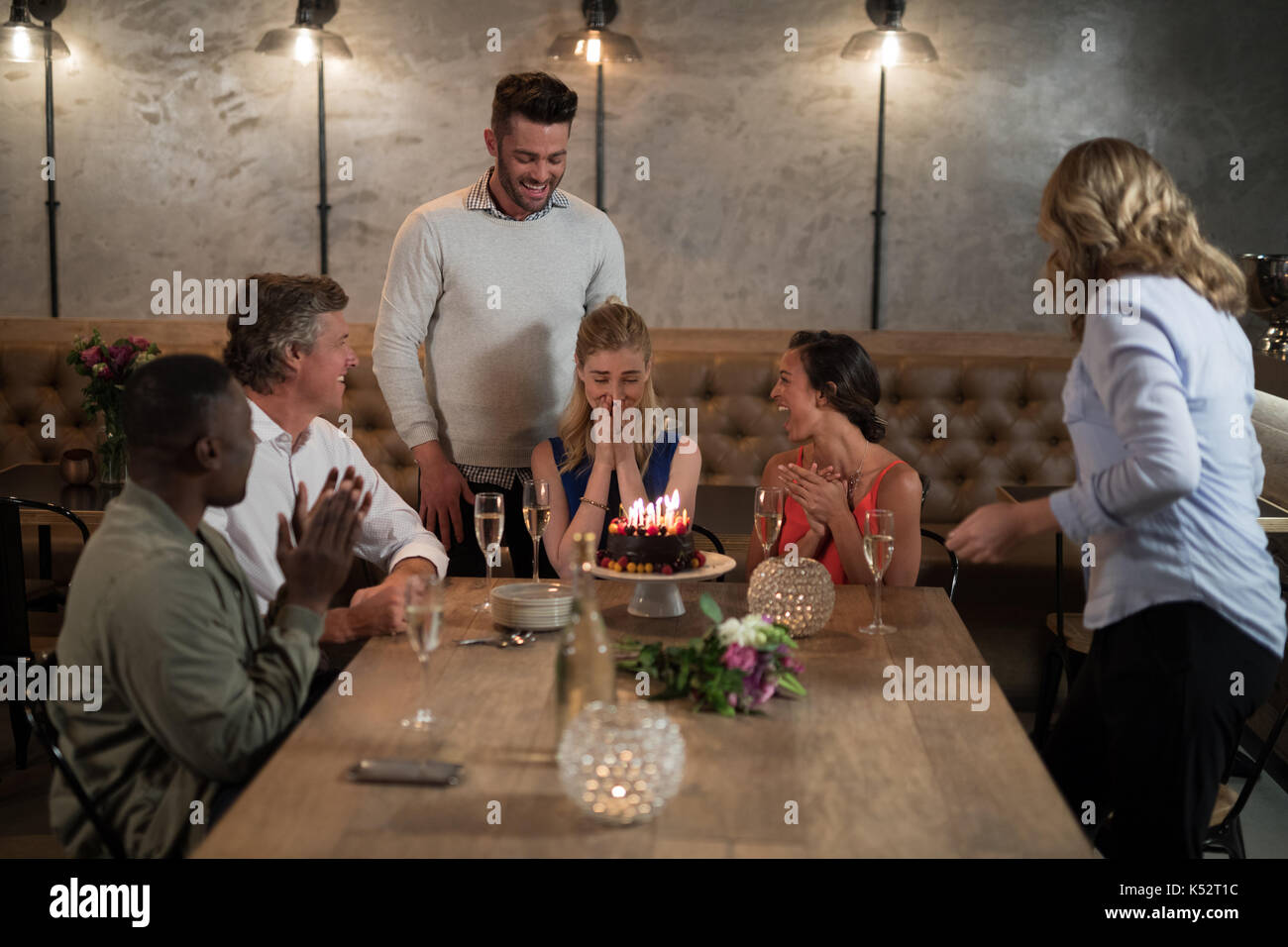 Woman receiving surprise birthday cake from her friends in restaurant Stock Photo