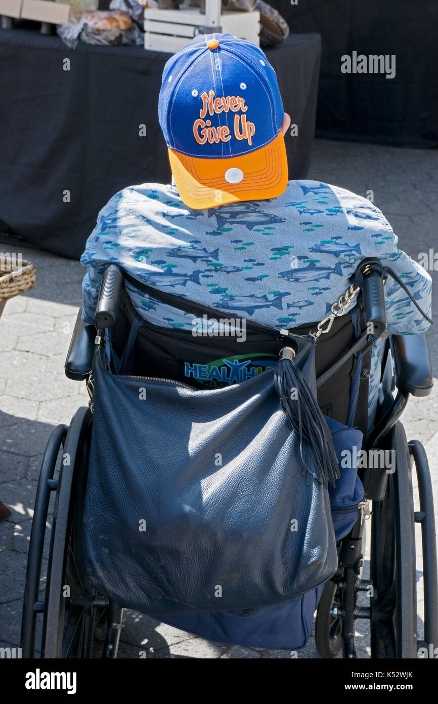 A man in a wheelchair wearing a cap with the slogan "Never Give Up Hope." In lower Manhattan, New York City. Stock Photo