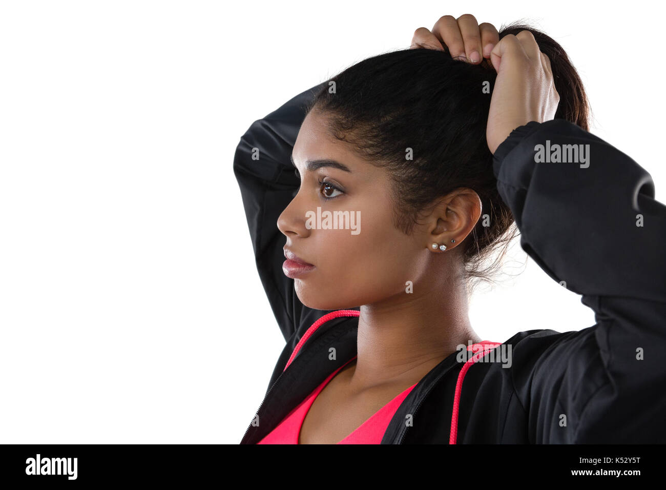 Young female athlete looking away while tying hair against white background Stock Photo