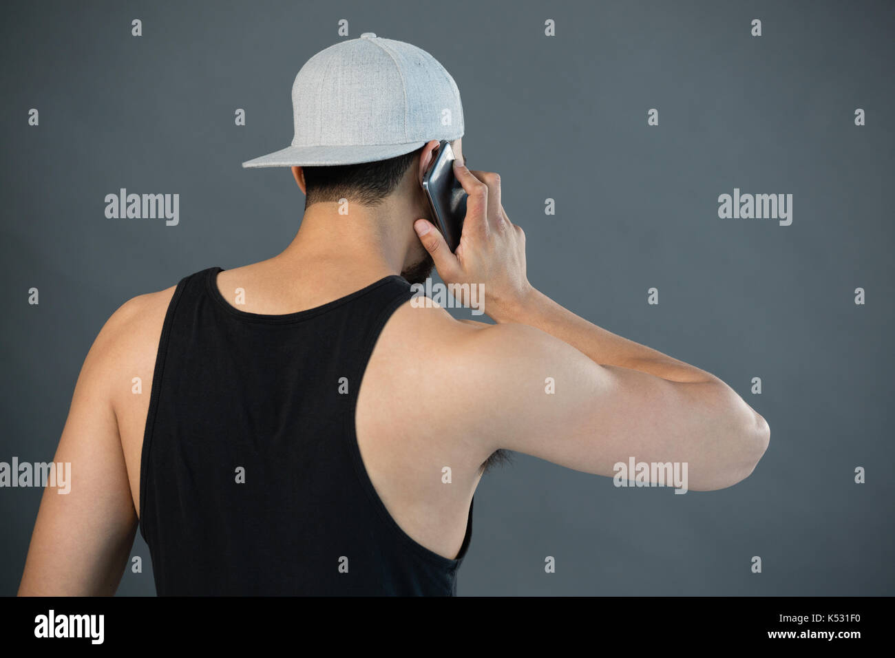 Rear view of man talking on mobile phone against grey background Stock ...