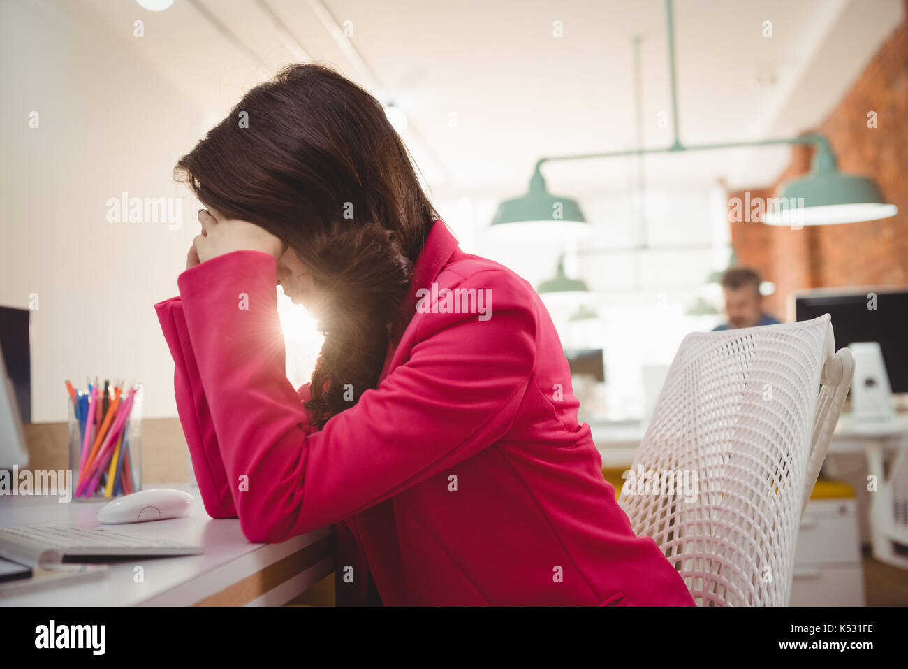 Tired female executive sitting with hands on forehead at desk in office Stock Photo