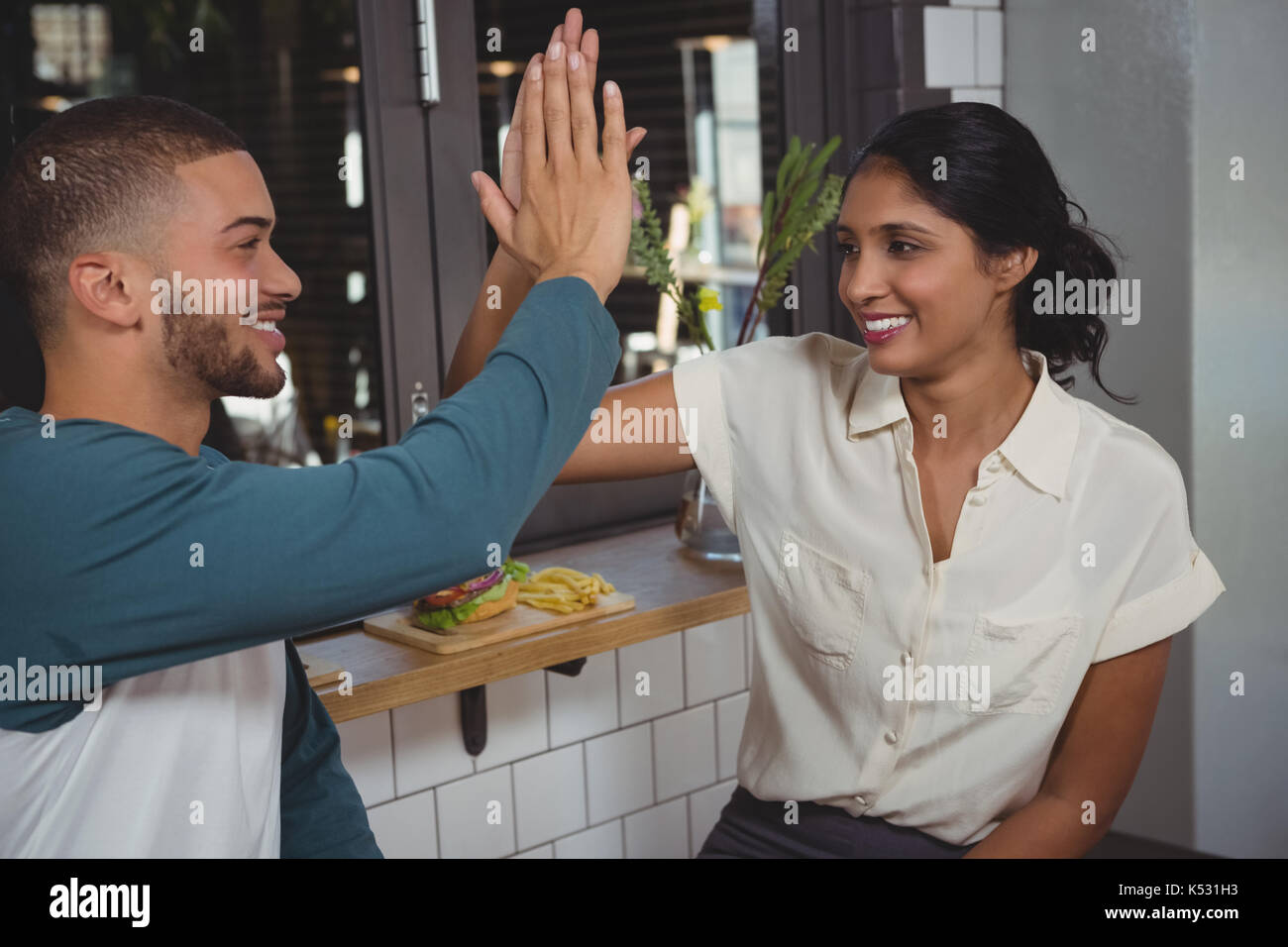 Happy young couple giving high-five while sitting in cafe Stock Photo
