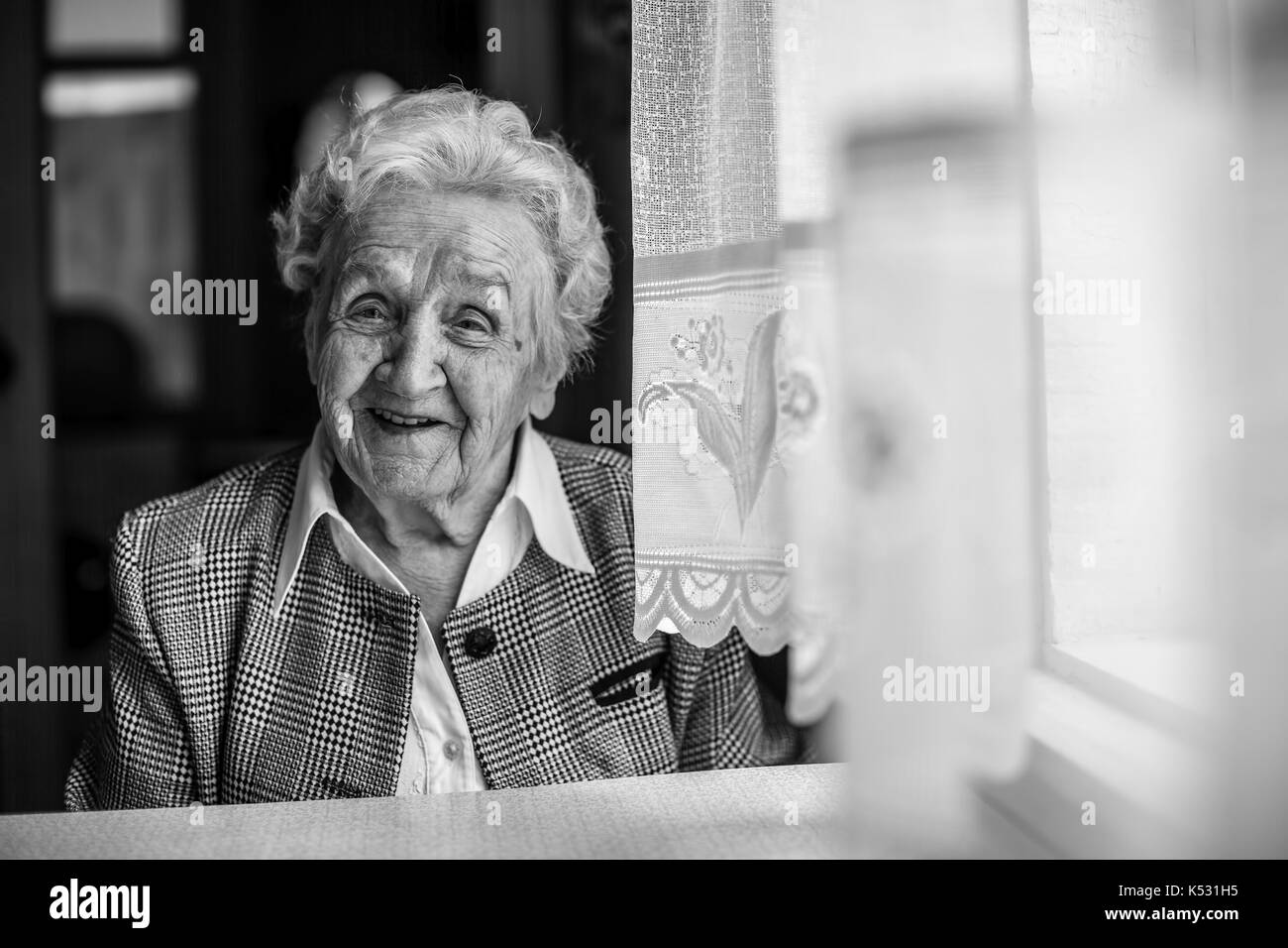 An elderly woman black and white portrait near the window. Stock Photo
