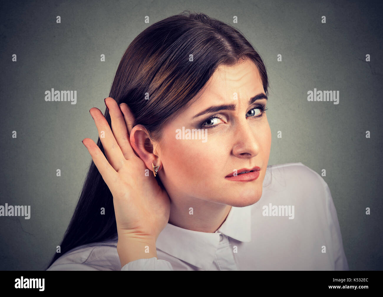 Woman with a hearing loss cupping her hand behind ear with her head turned towards camera to try and amplify available sound Stock Photo