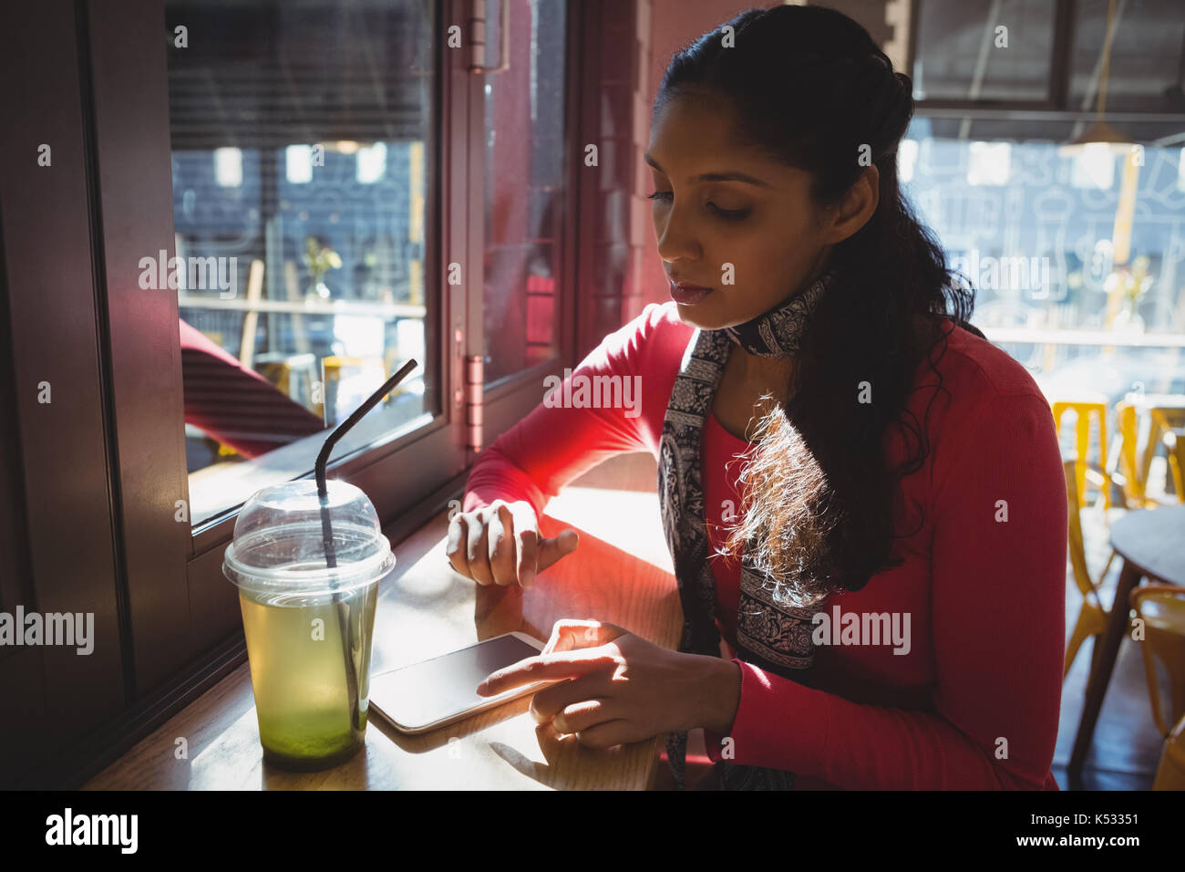 Young woman with drink using phone at window sill in cafe Stock Photo