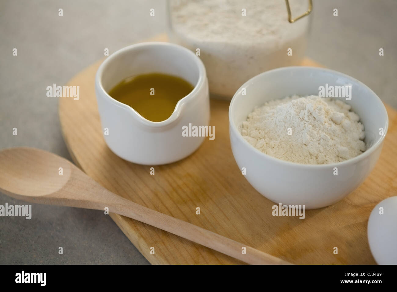 Flour and oil in containers on cutting board at table Stock Photo