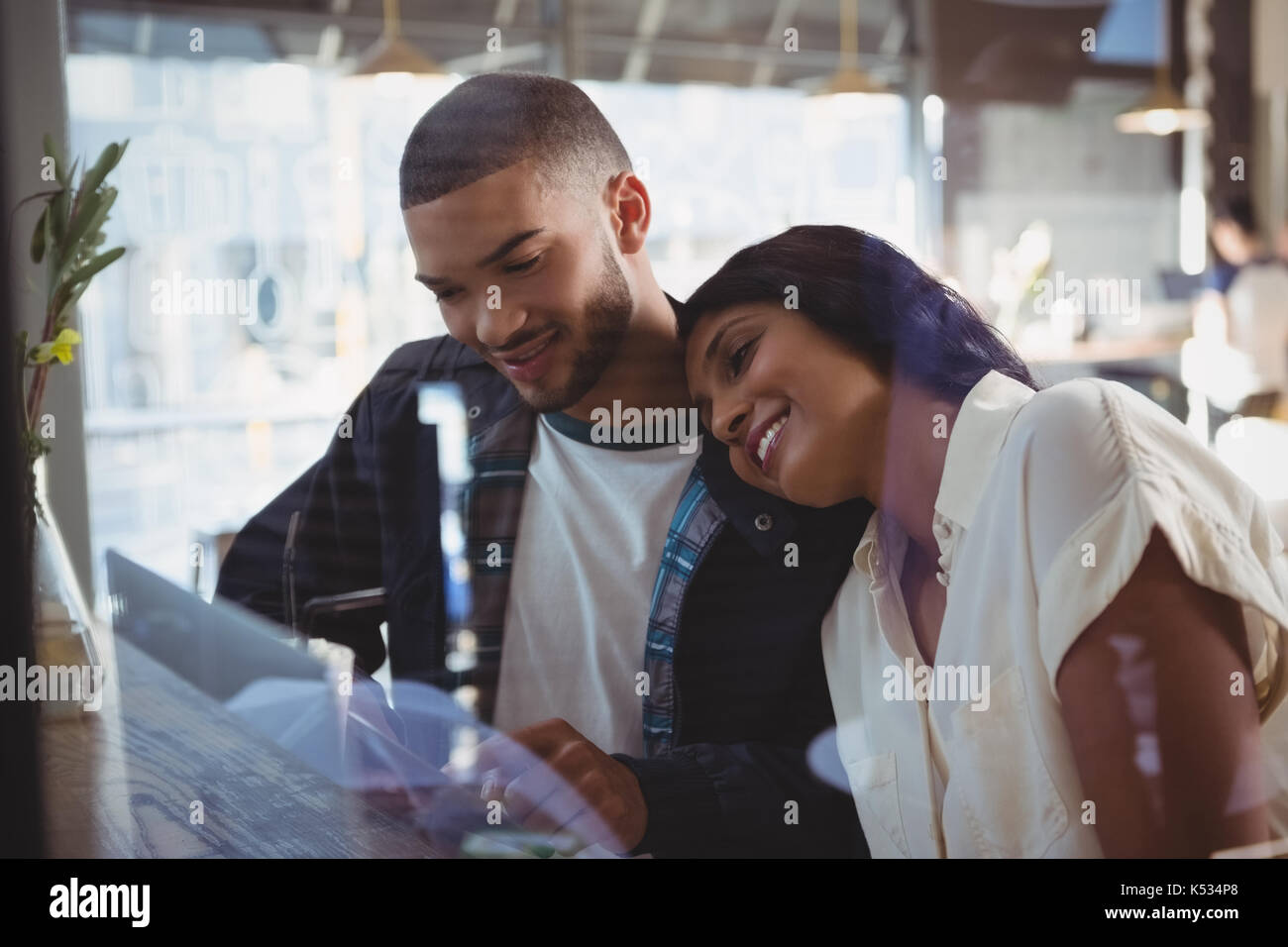 Young woman leaning on man shoulder seen through glass in cafe Stock Photo