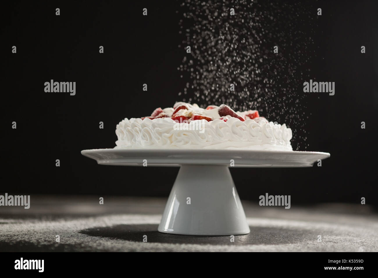Powdered sugar falling over white cake on stand against black background Stock Photo
