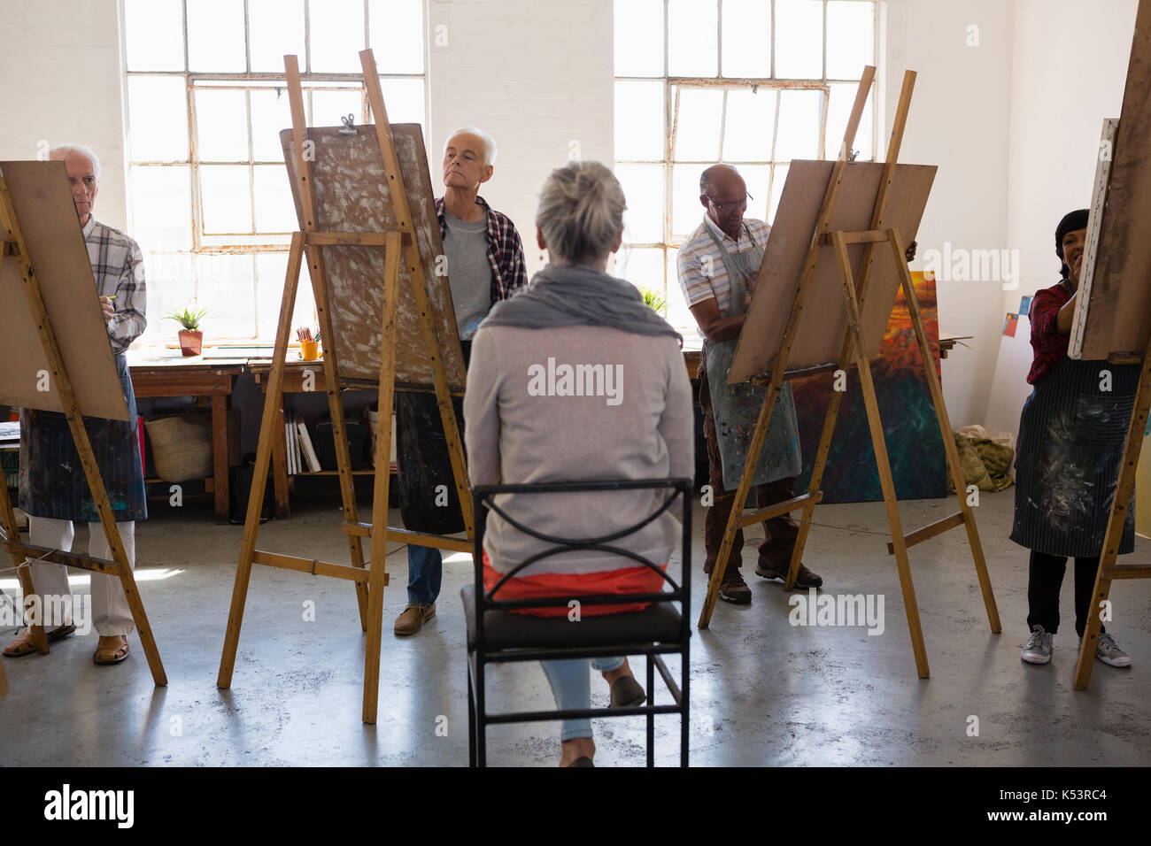 Rear view of woman sitting on chair while artist sketching in art class ...