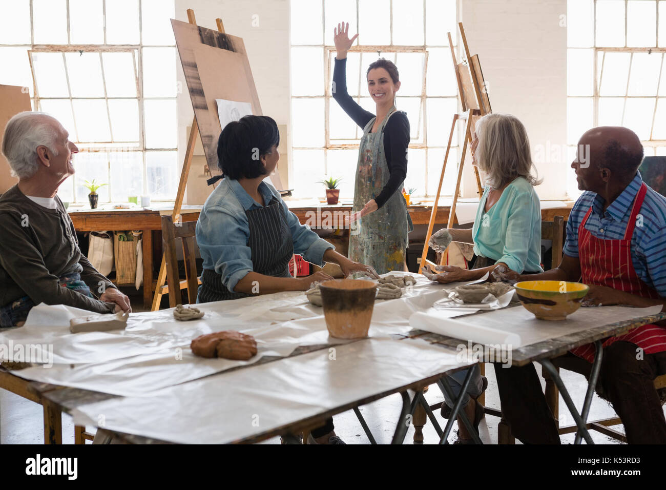 Senior man and woman looking at female instructor gesturing while standing in art class Stock Photo