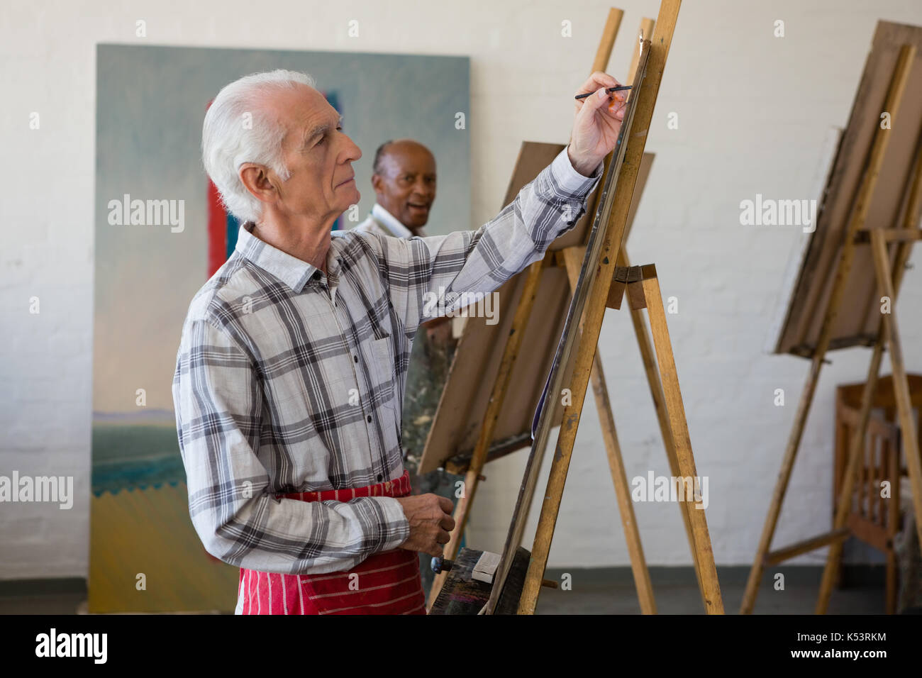 Side view of senior man painting on easel in art class Stock Photo - Alamy