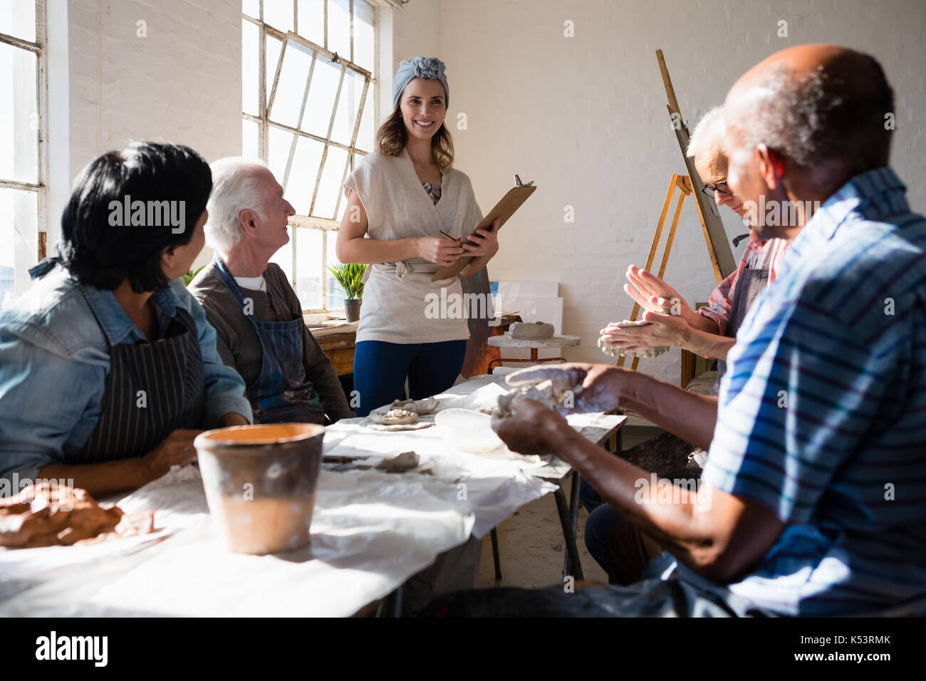 Smiling teacher looking at senior adults at table in  art class Stock Photo
