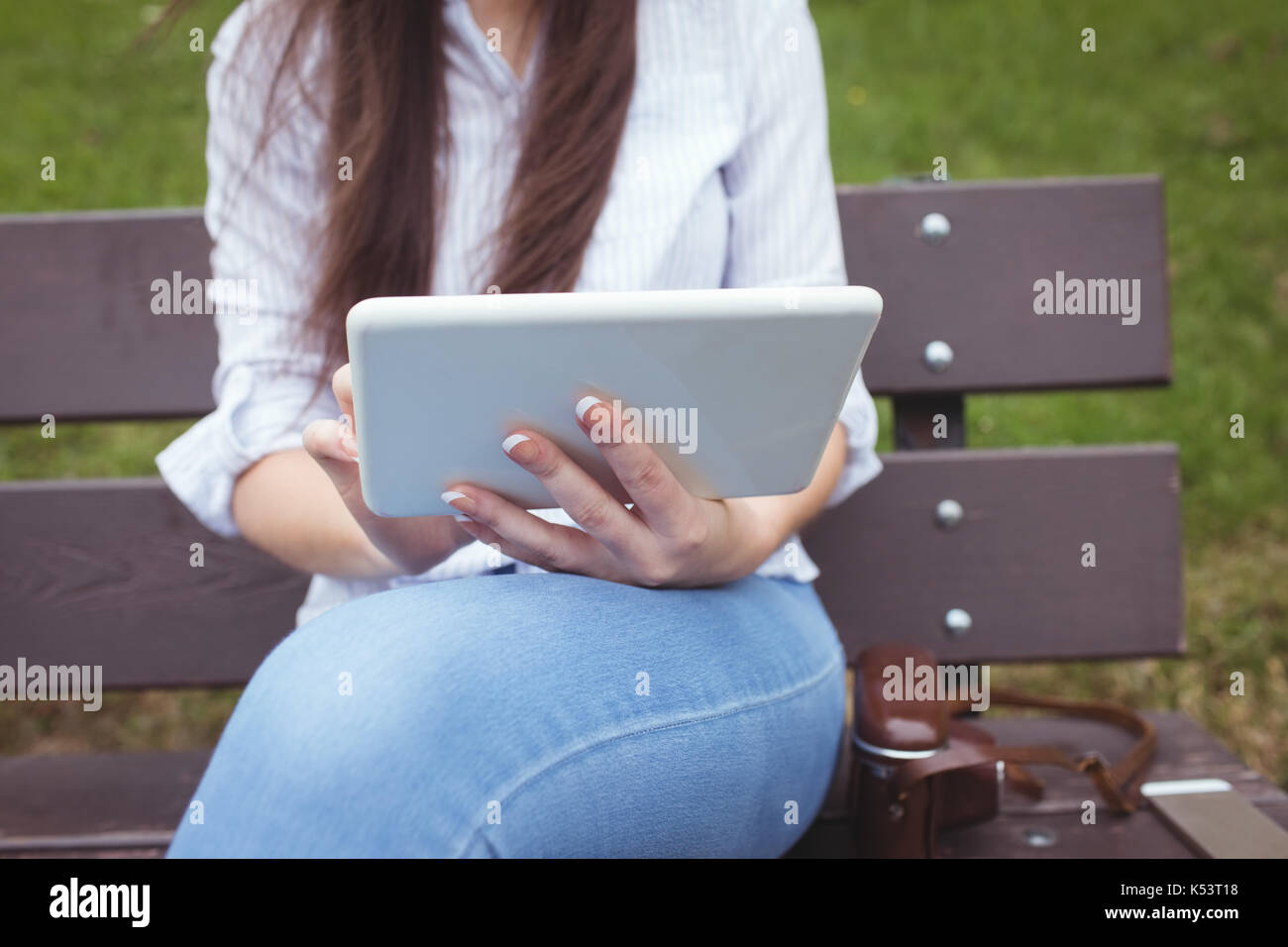 Mid-section of woman sitting on bench and using digital tablet in forest Stock Photo