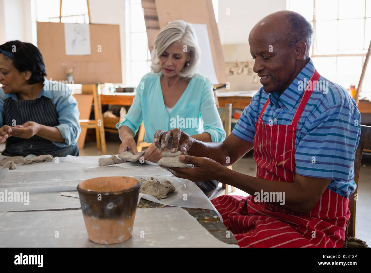 Senior friends making clay products while sitting at table in art class Stock Photo