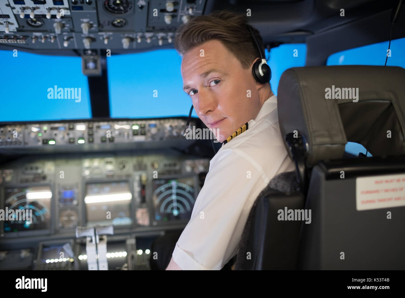 Portrait of handsome young male pilot wearing headphones while sitting on seat in airplane cockpit Stock Photo