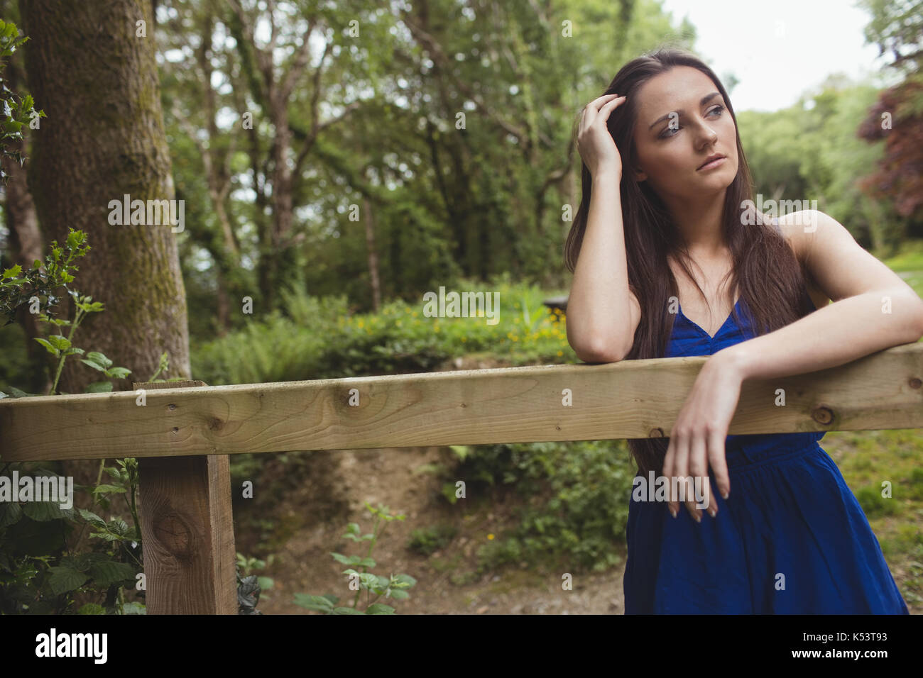 Thoughtful woman leaning on wooden fence in forest Stock Photo