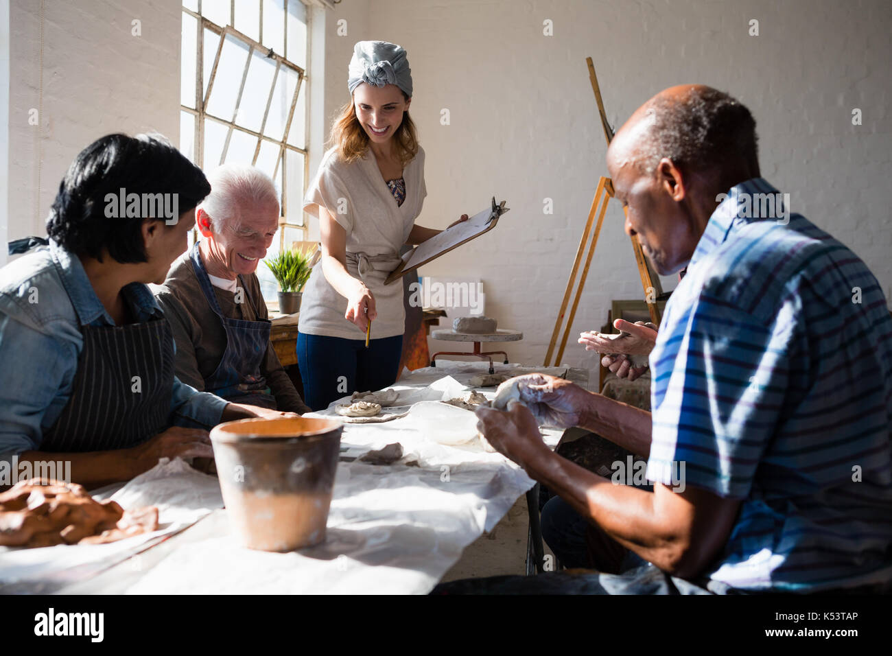 Smiling teacher assisting senior adults at table in  art class Stock Photo