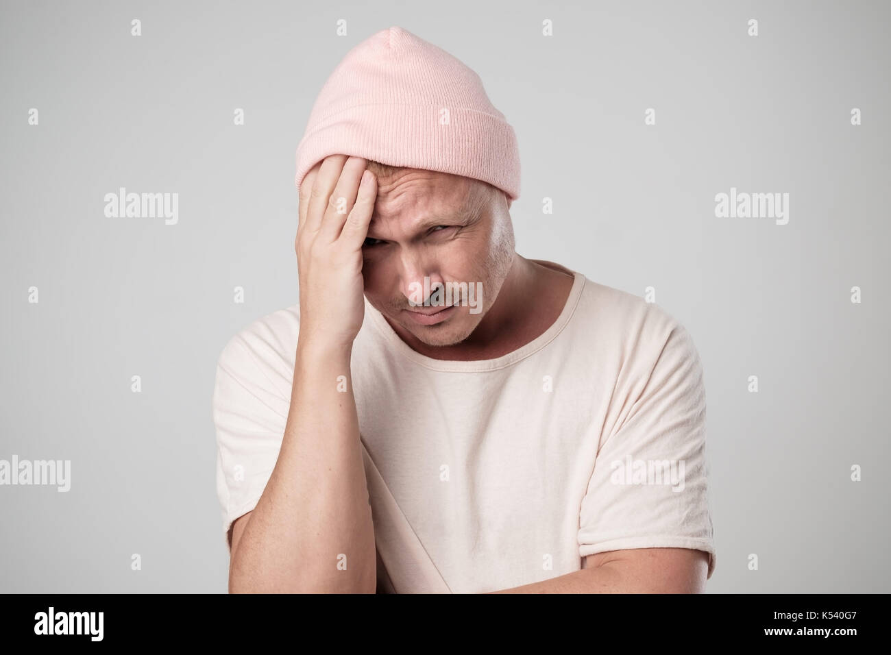 Portrait of sad caucasian man in pink hat. He holds head because of pain and looks down. Concept of body language Stock Photo