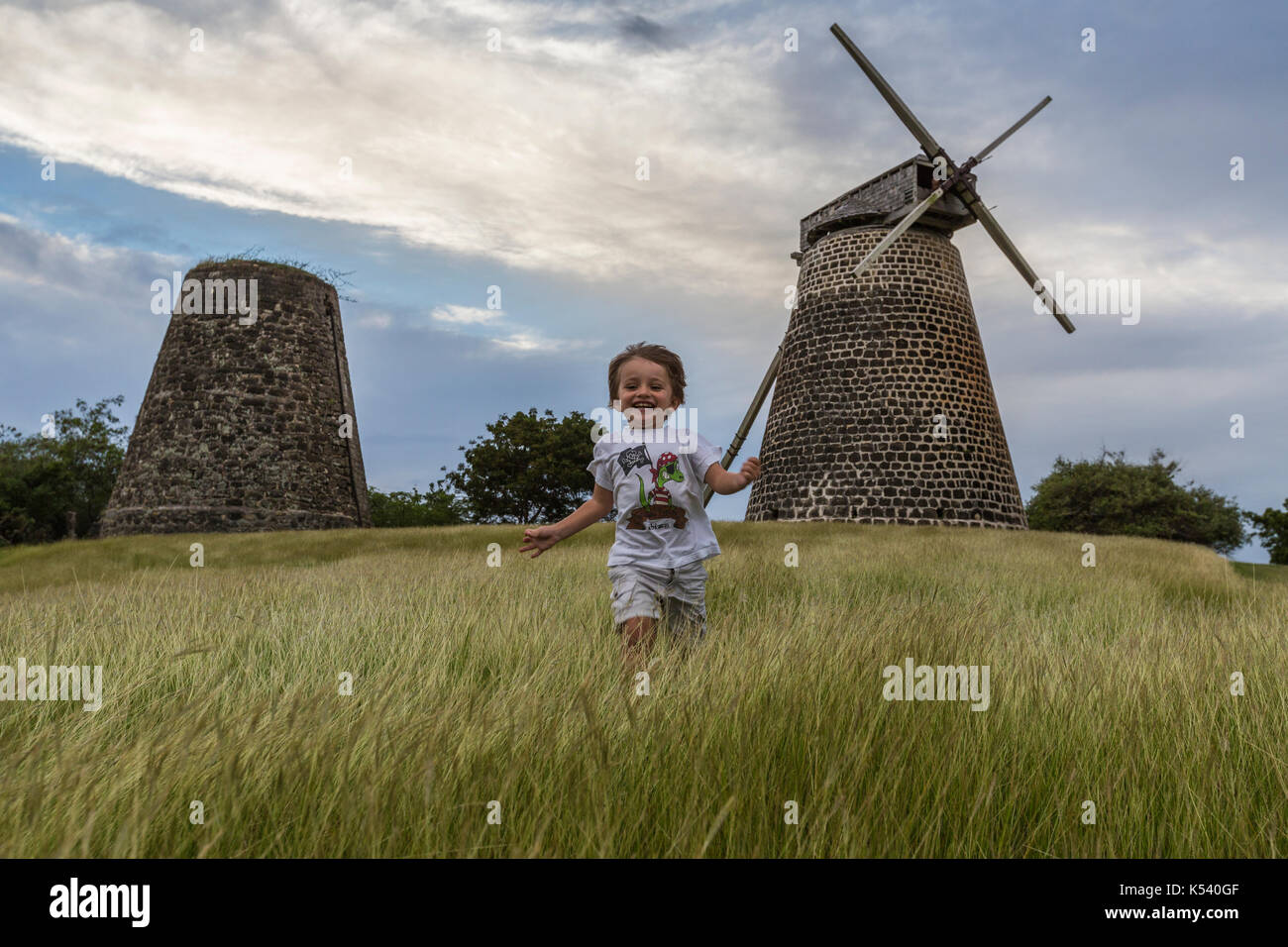 Child runs on green meadows with windmills on background, Betty's Hope, Antigua Stock Photo