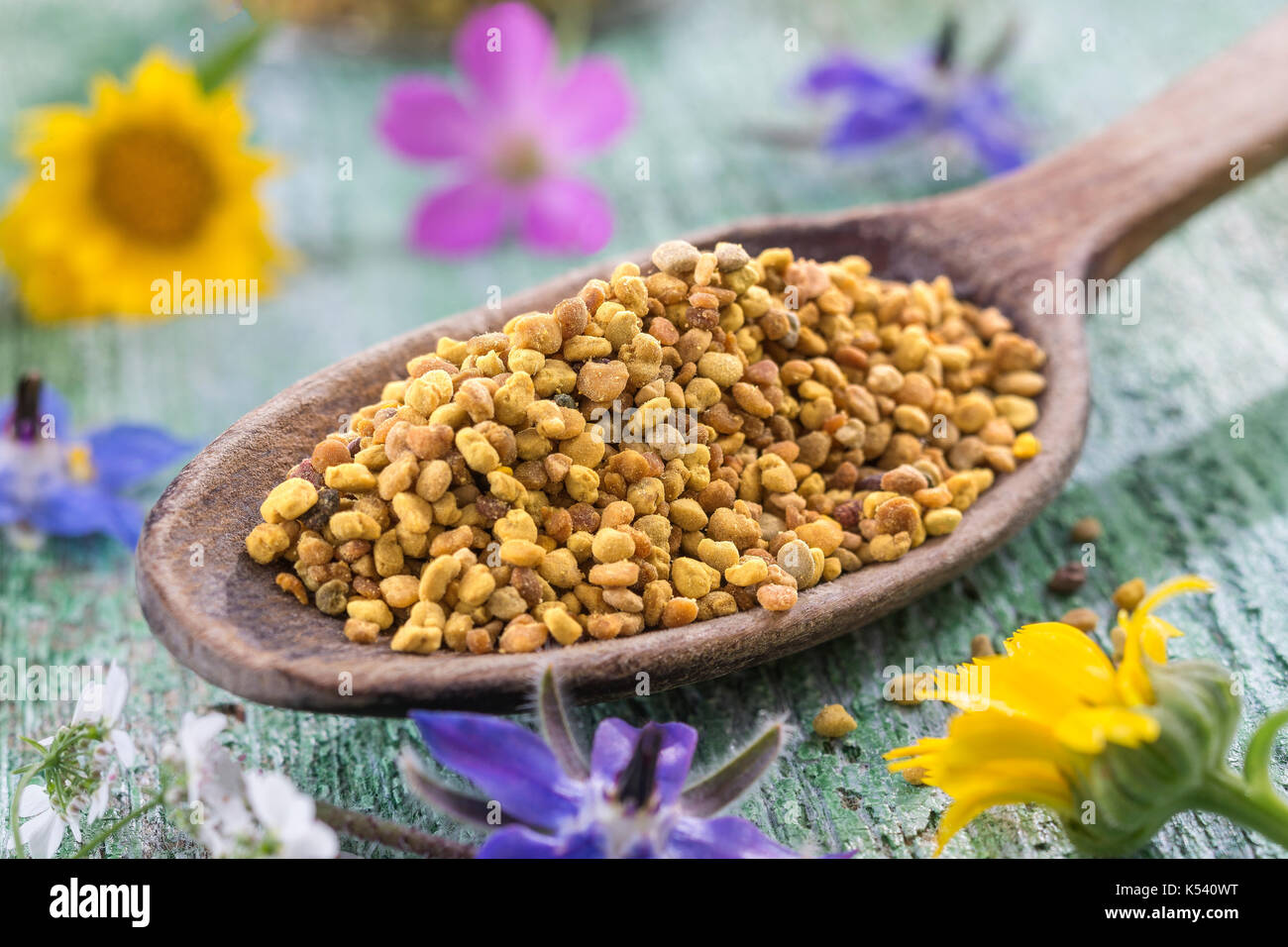 Wooden spoon with pollen on the table surrounded by flowers Stock Photo