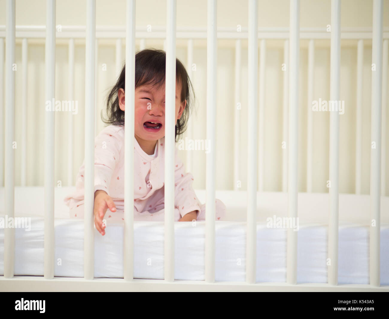 Baby girl crying in cot bed Stock Photo Alamy