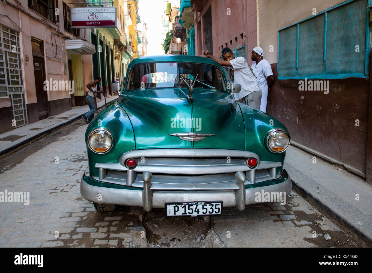 Two men hang out near their 1950 Chevrolet car on a street in the middle of Havana, Cuba in the Caribbean. Stock Photo