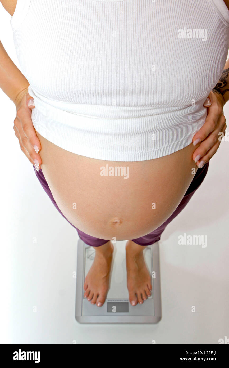 Pregnant woman controls her weight on a body scale Stock Photo