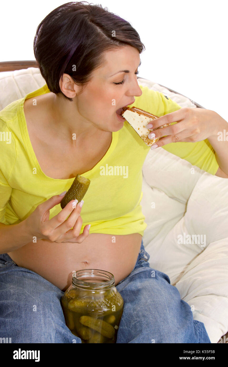 Pregnant woman eating a piece of sweet cake and sour pickle together Stock Photo