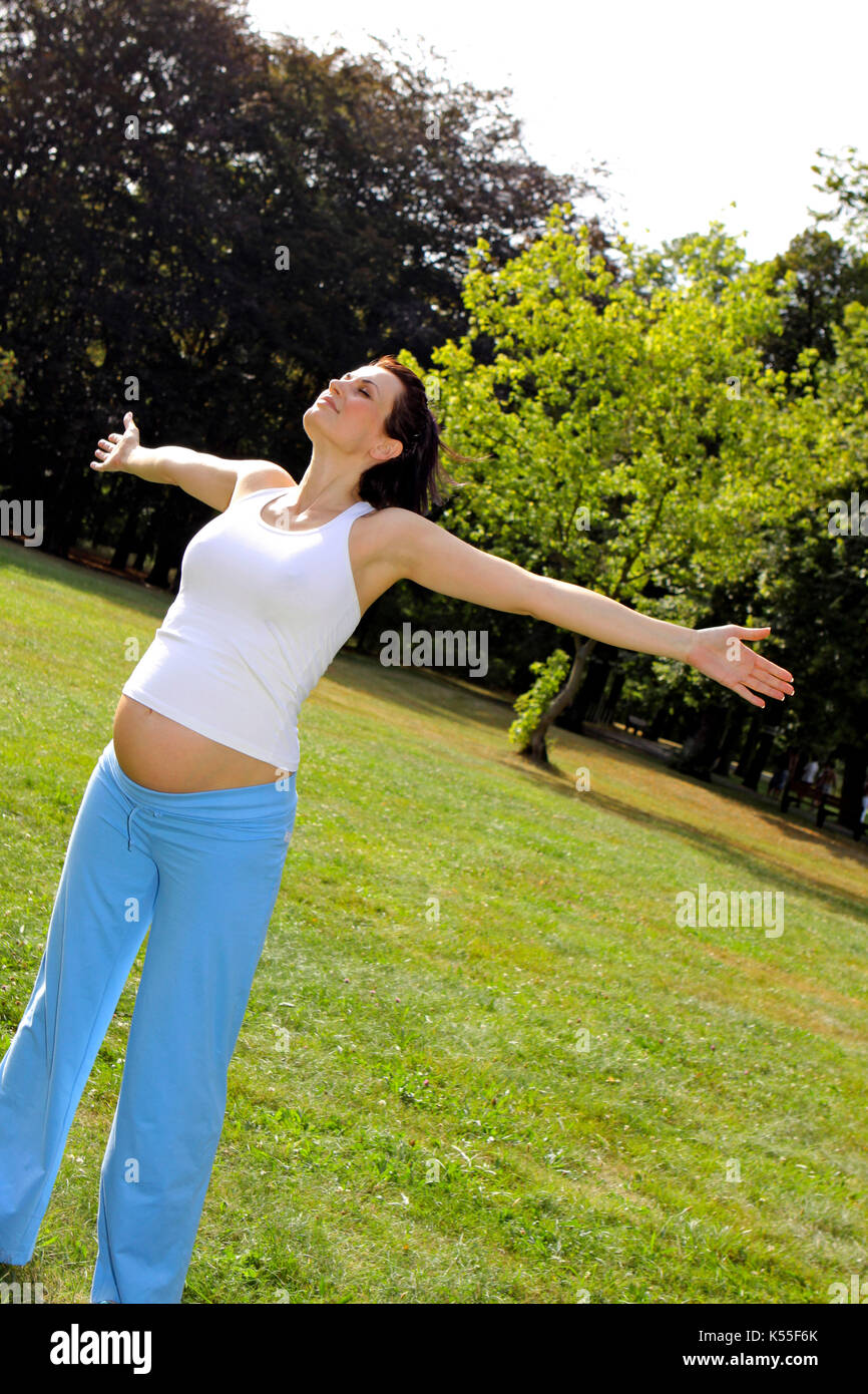 Pregnant woman doing gymnastics exercises in a park in summer Stock Photo