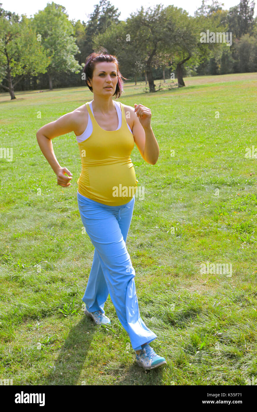 Pregnant woman doing exercises, walking in a park in summer Stock Photo