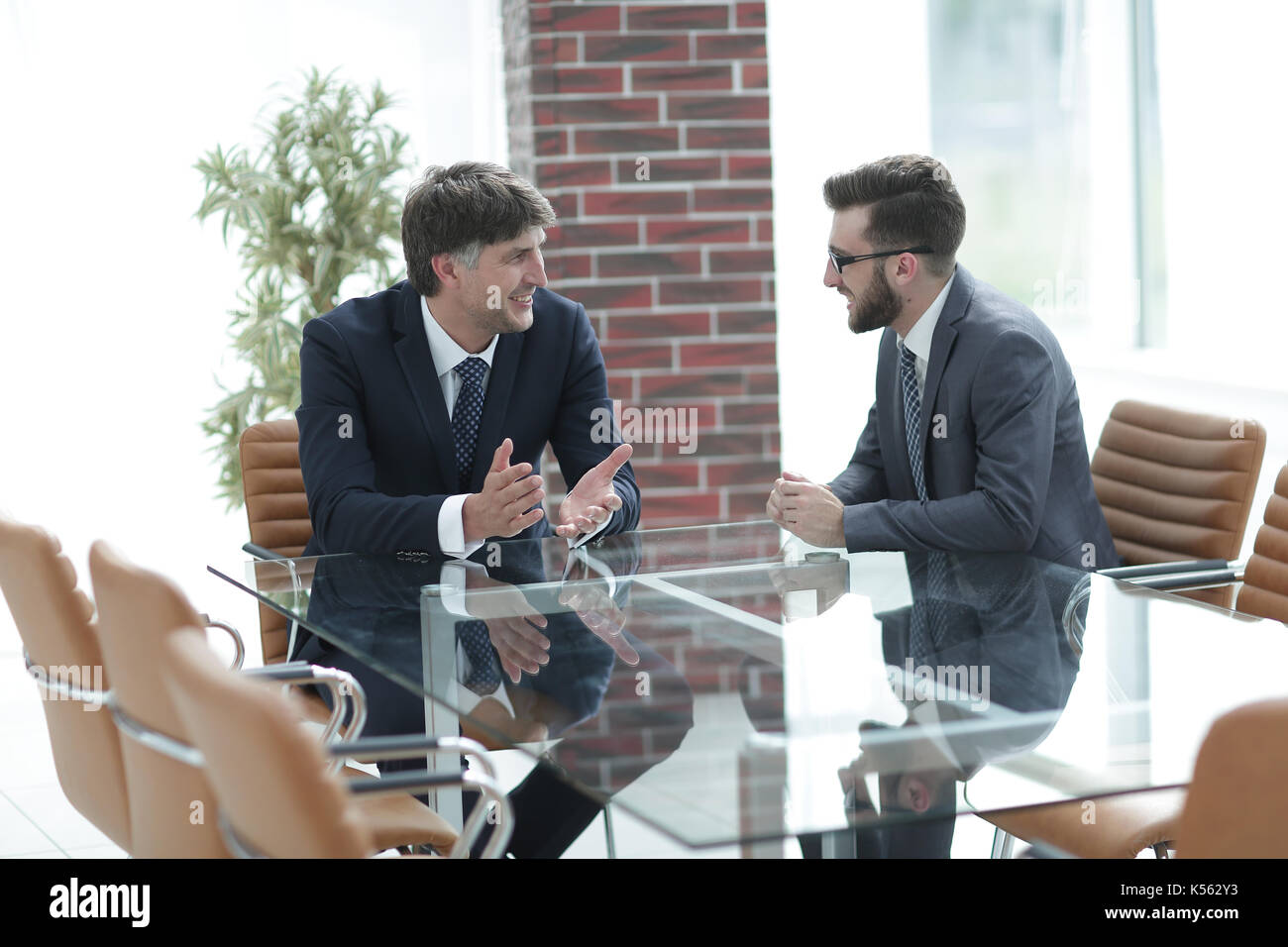 Two businessmen discussing tasks sitting at office table. Stock Photo