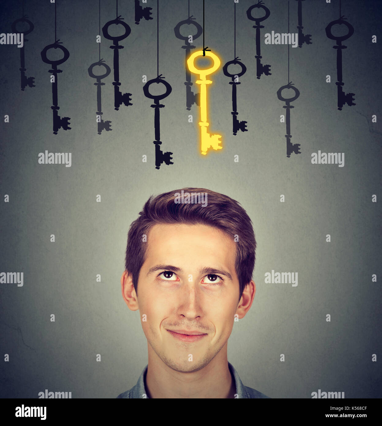 Thoughtful man looking up at vintage golden key to success among many others hanging. Concept of business aspirations, achievement Stock Photo