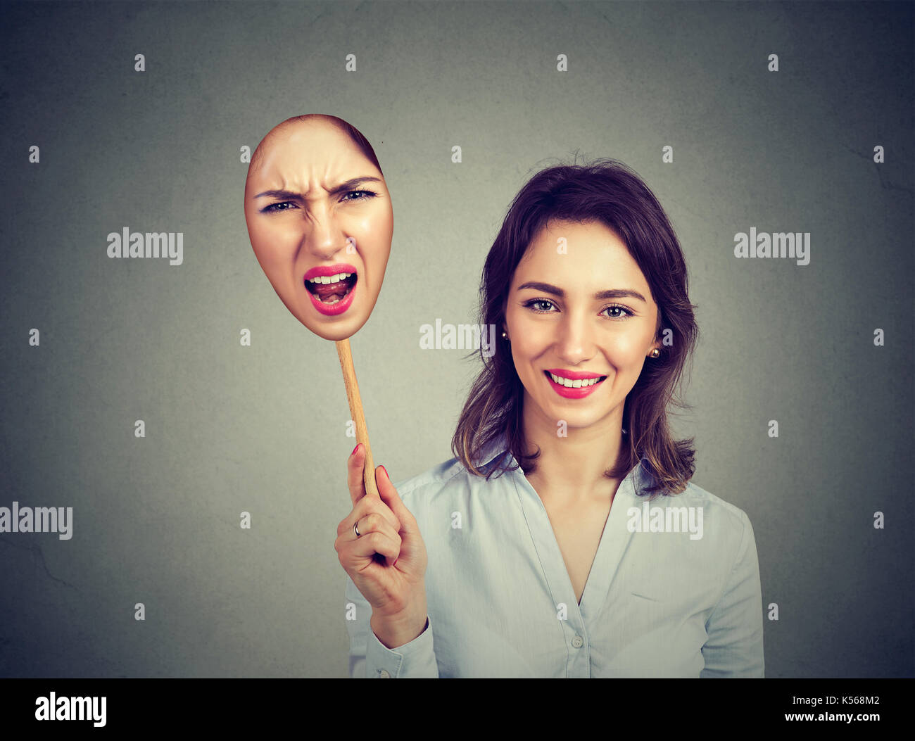 Happy smiling woman taking off an angry mask of herself Stock Photo