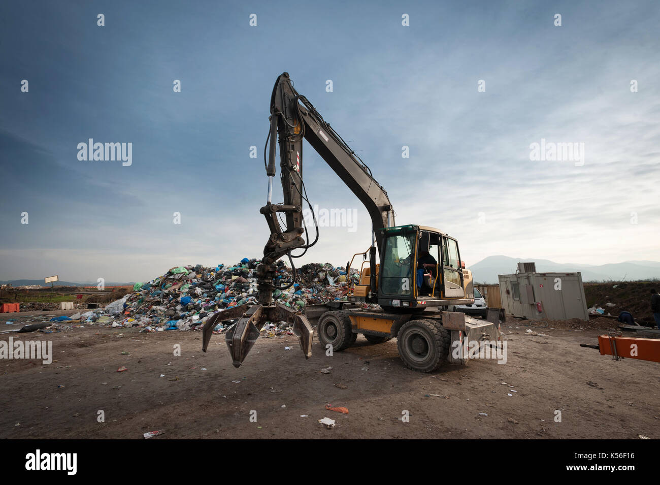 Bulldozer with mechanical arm grabbing waste from a pile at city landfill. Waste management, ecology concept. Stock Photo