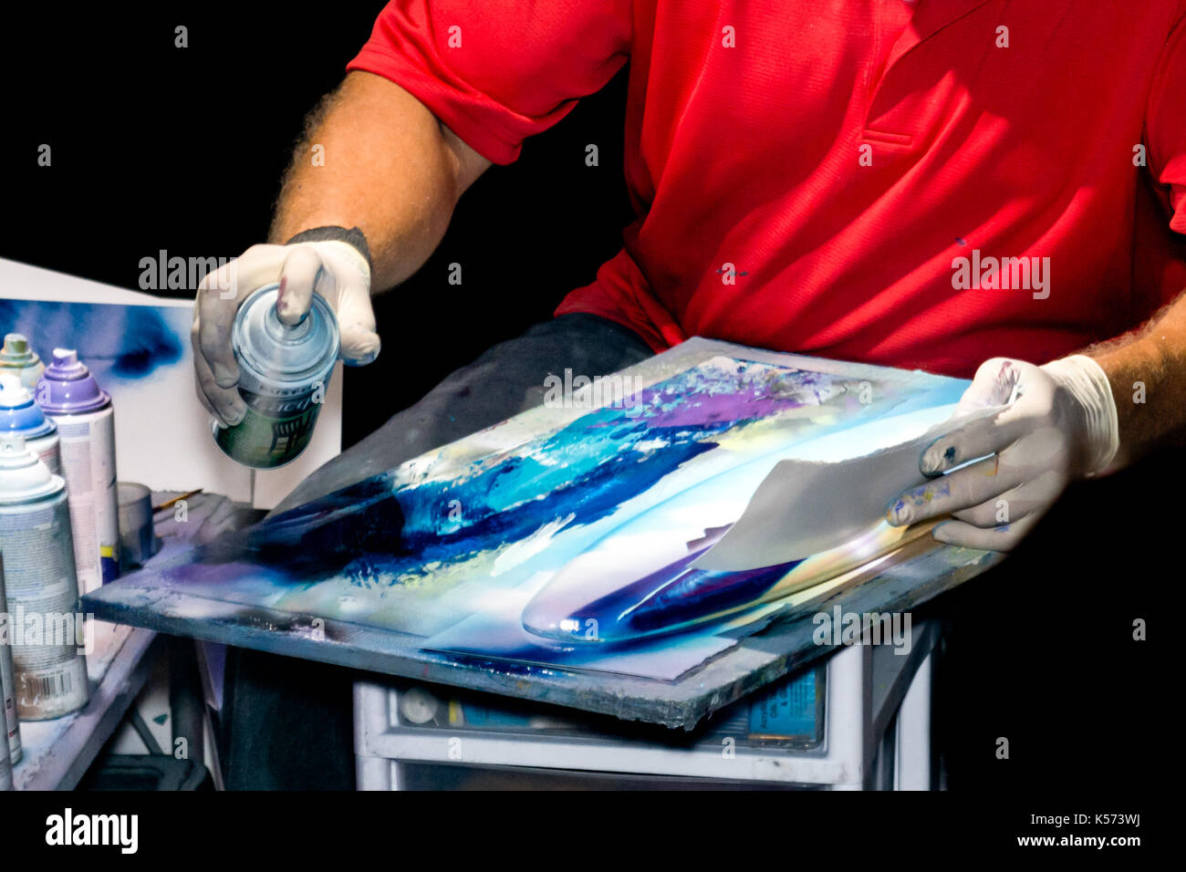 Street Artist spray painting souvenir surfboards. Painter's hands covered in latex gloves. Stock Photo
